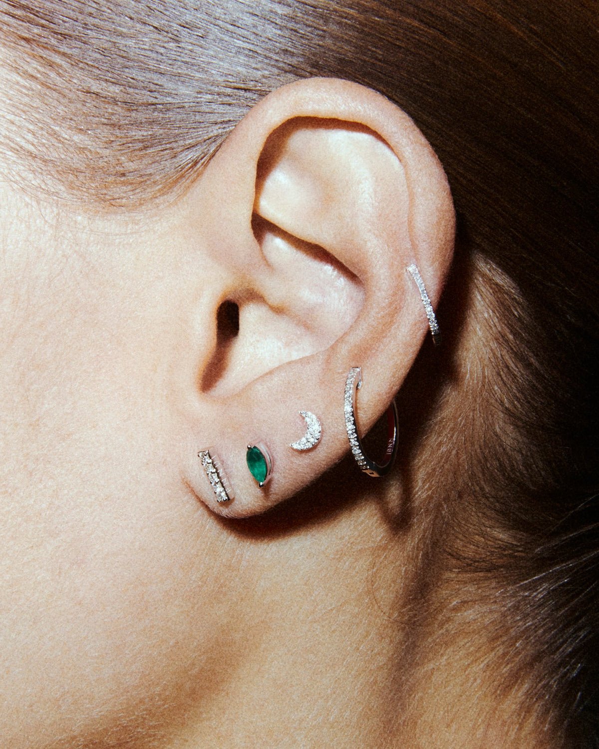 Awareness labret in 14k white gold, set with an emerald, shown on the ear.
