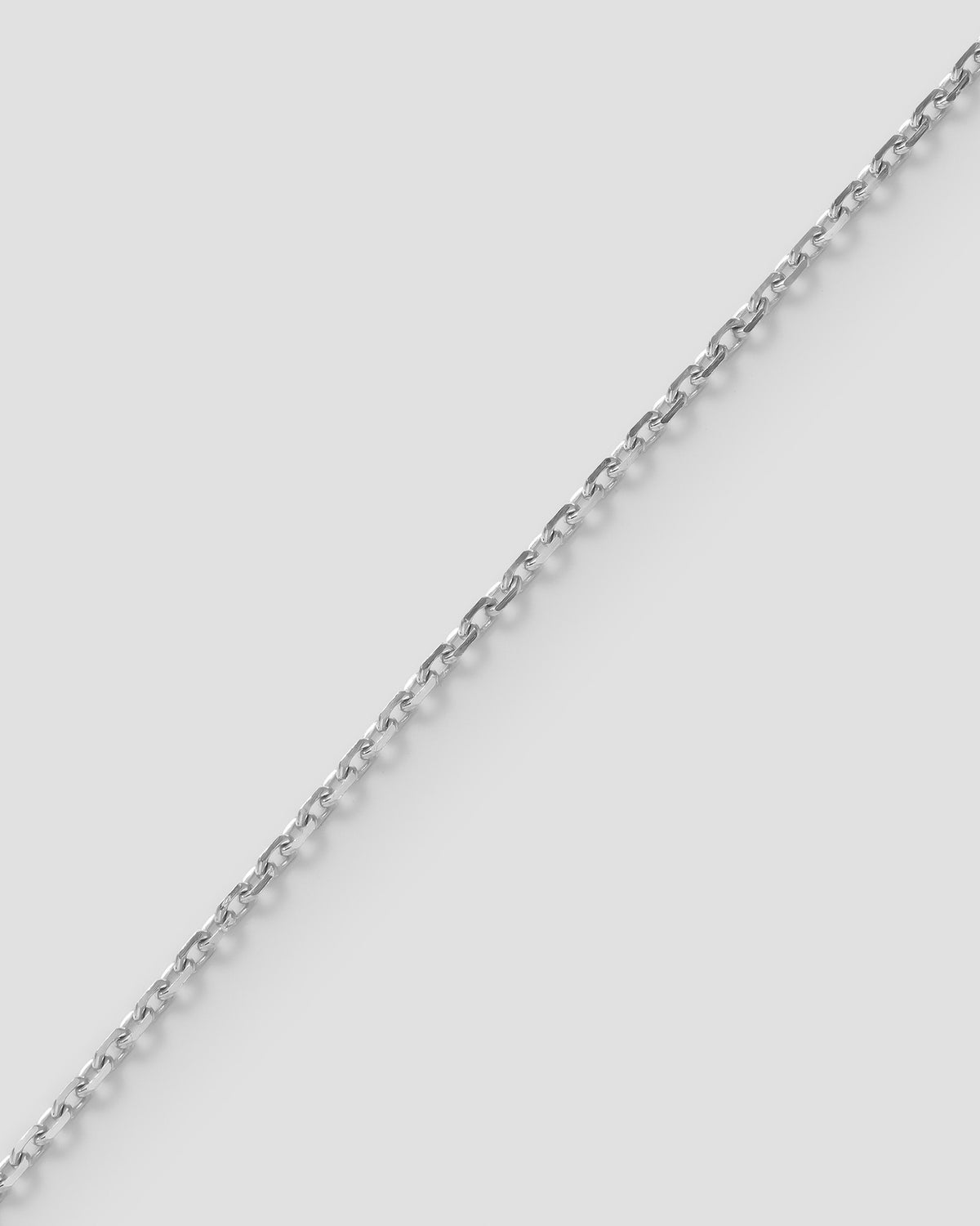 Diamond cut mirror chain, 1.0 mm, in 18k white gold, laid diagonally on a pale ground.