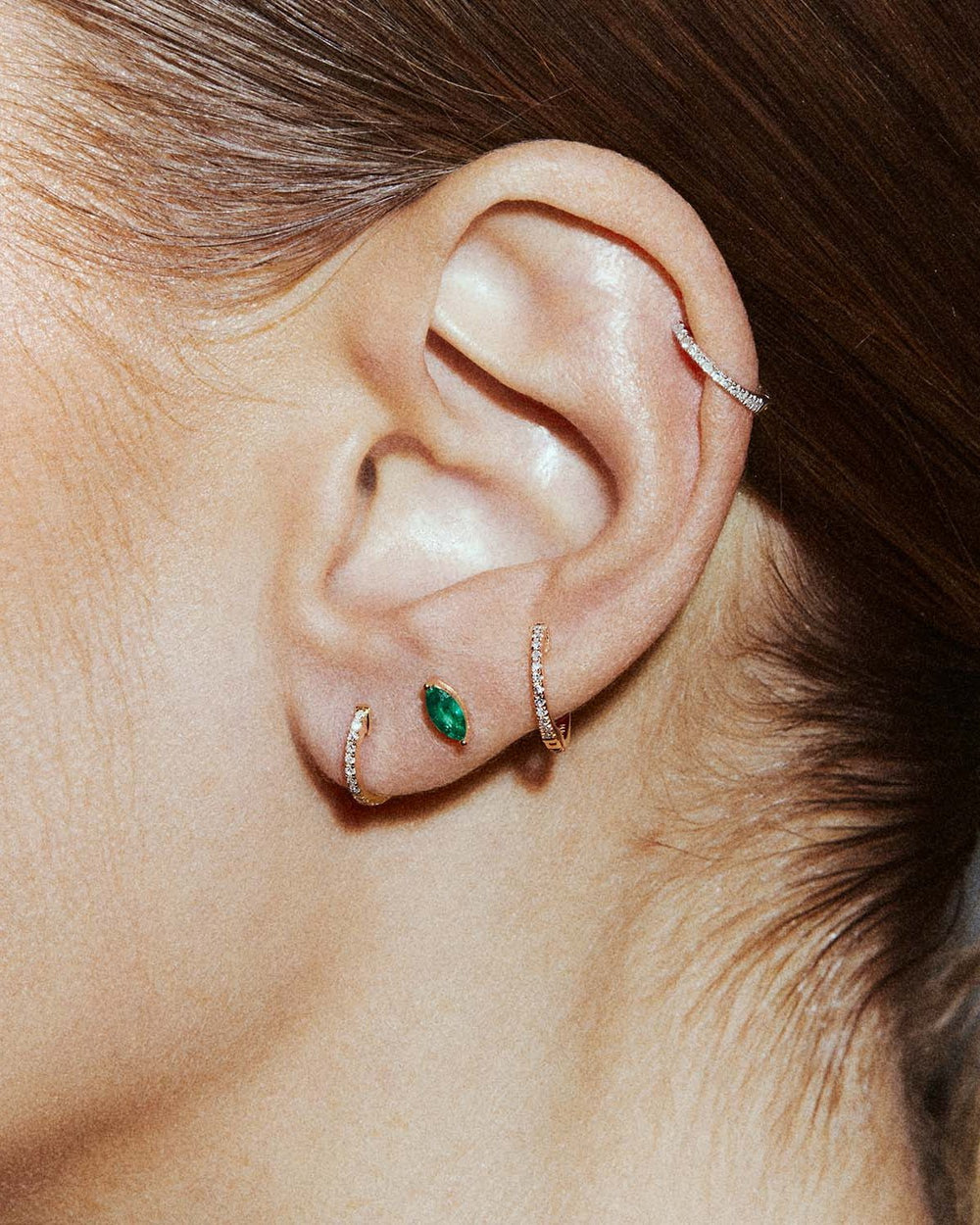 Awareness labret in 14k yellow gold, set with an emerald, shown on the ear.