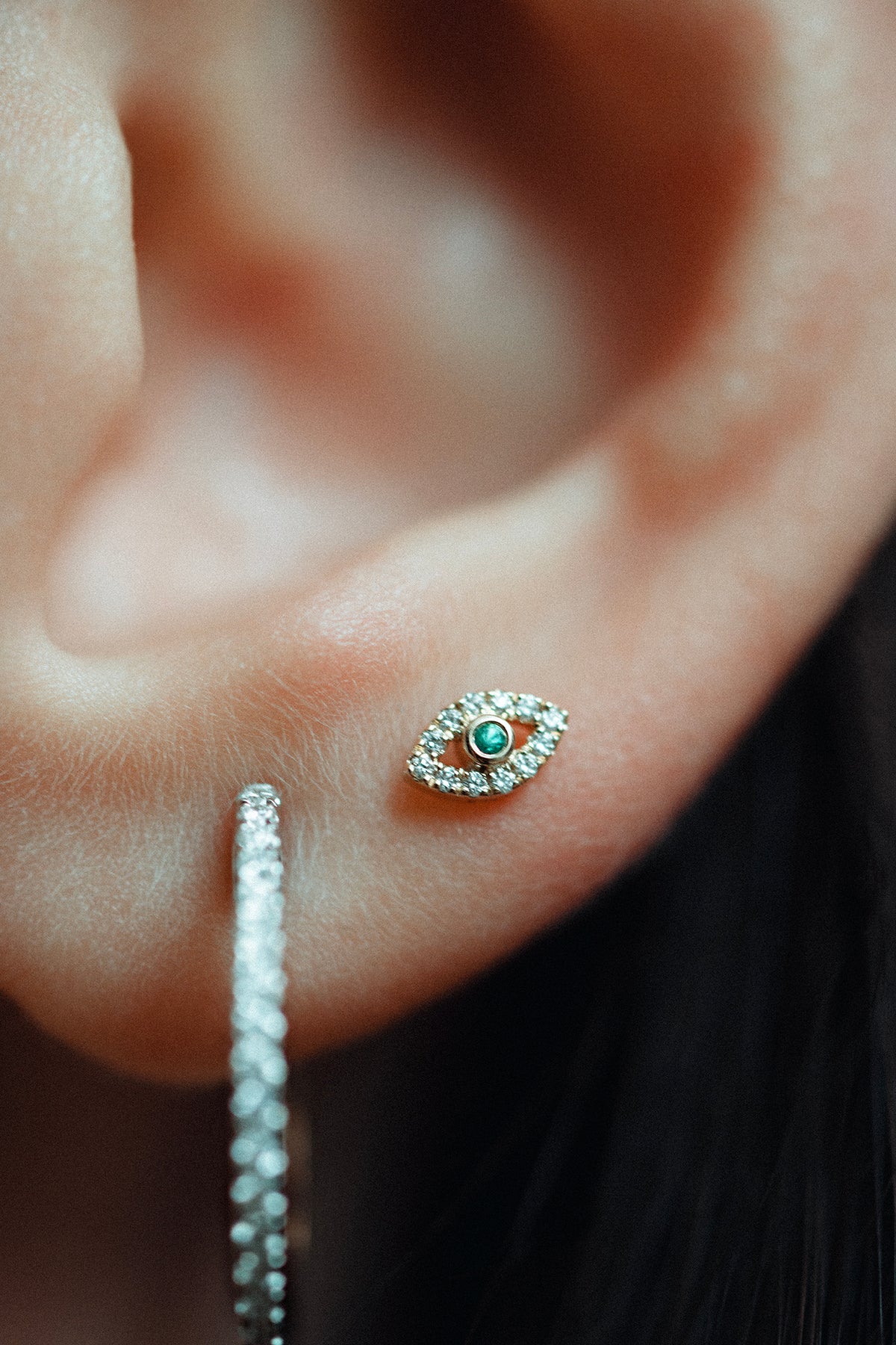 Eirene eye stud in 14k yellow gold, set with an emerald and natural diamonds, shown on the ear.